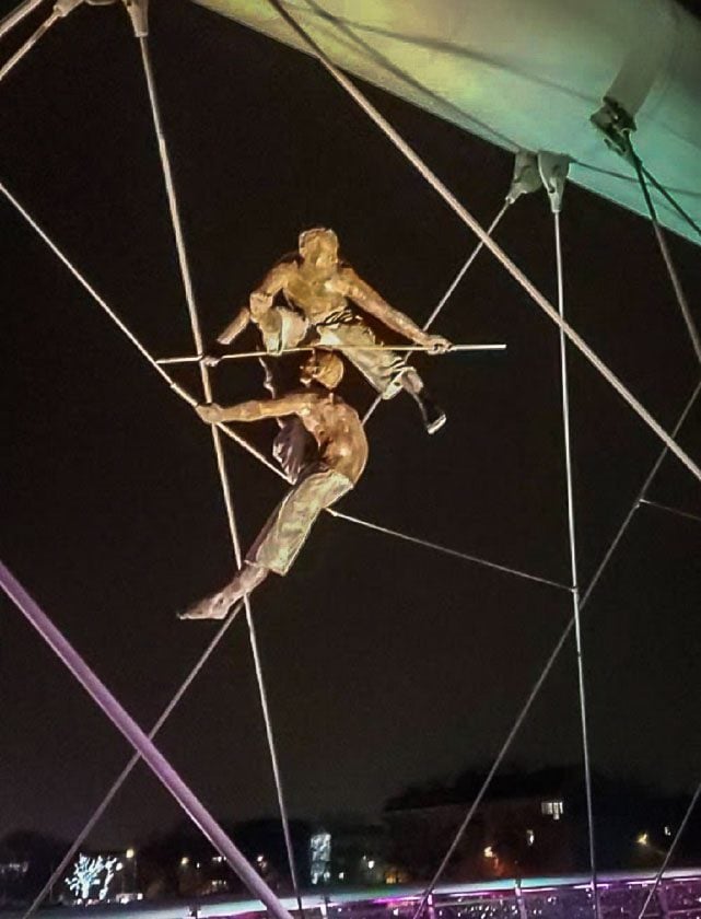 Circus actor statues posing in the bridge's cables