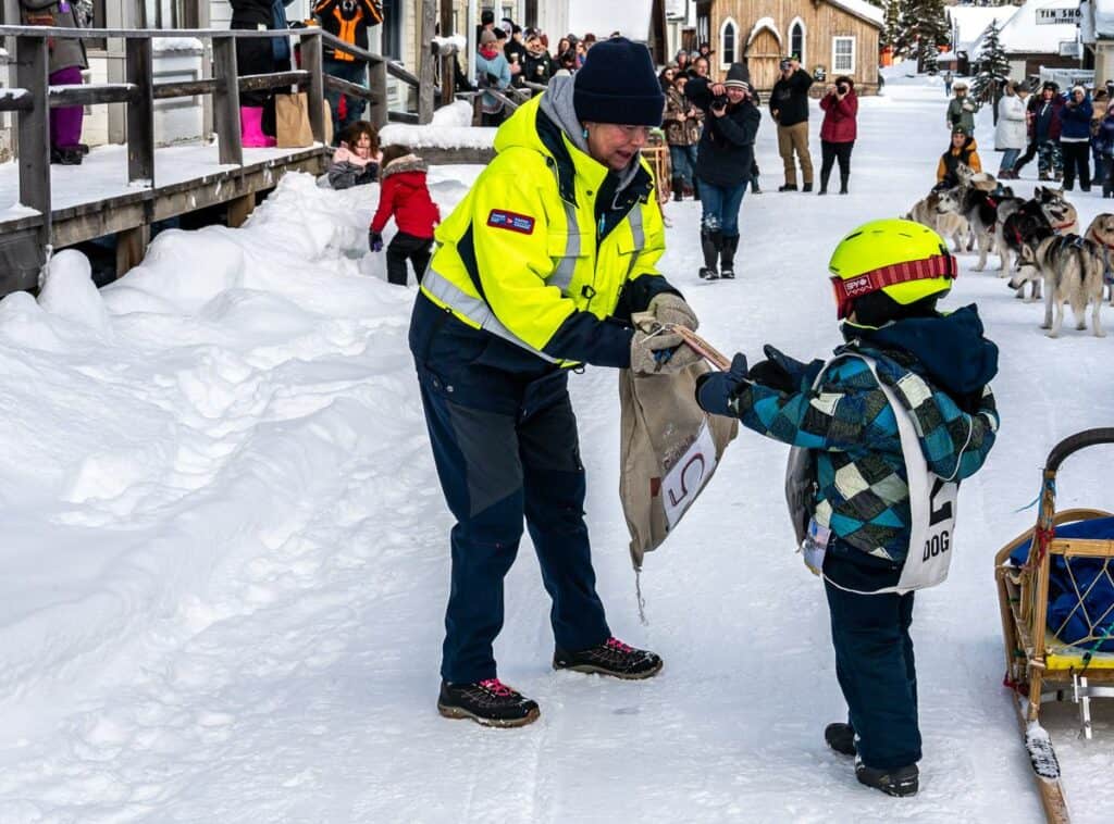 A young boy handing over the mail carried by the dog sleds in Barkerville